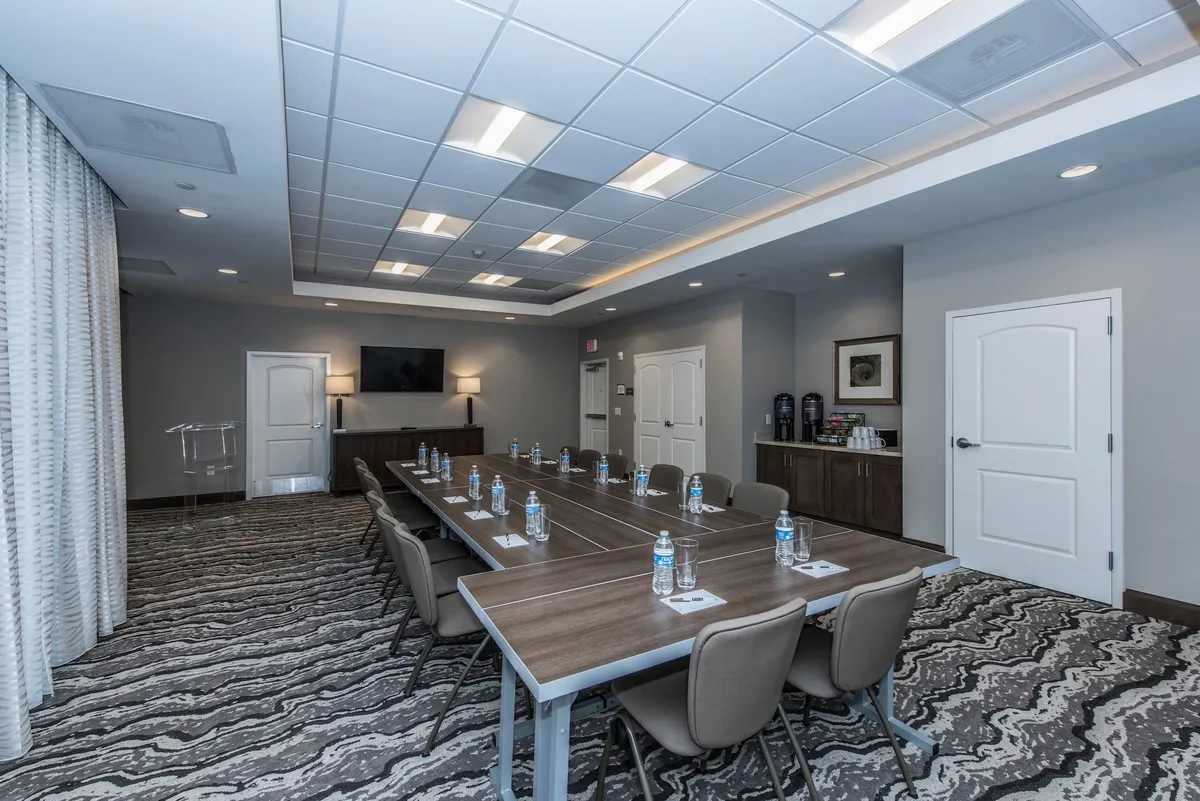 A sleek conference room featuring a long table, large screen TV, water bottles, and decorative wall art. The setting is ideal for formal meetings, presentations, or team brainstorming sessions, and exudes a focused, collaborative energy.