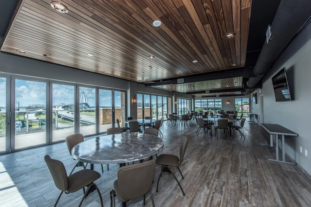 A sophisticated interior space with large windows offering scenic outside views, elegant circular tables ideal for meetings or social gatherings, and a stylish wooden ceiling that lends a contemporary yet relaxed mood.